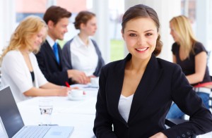 young woman dressed in business attire with staff members sitting blurred in the background