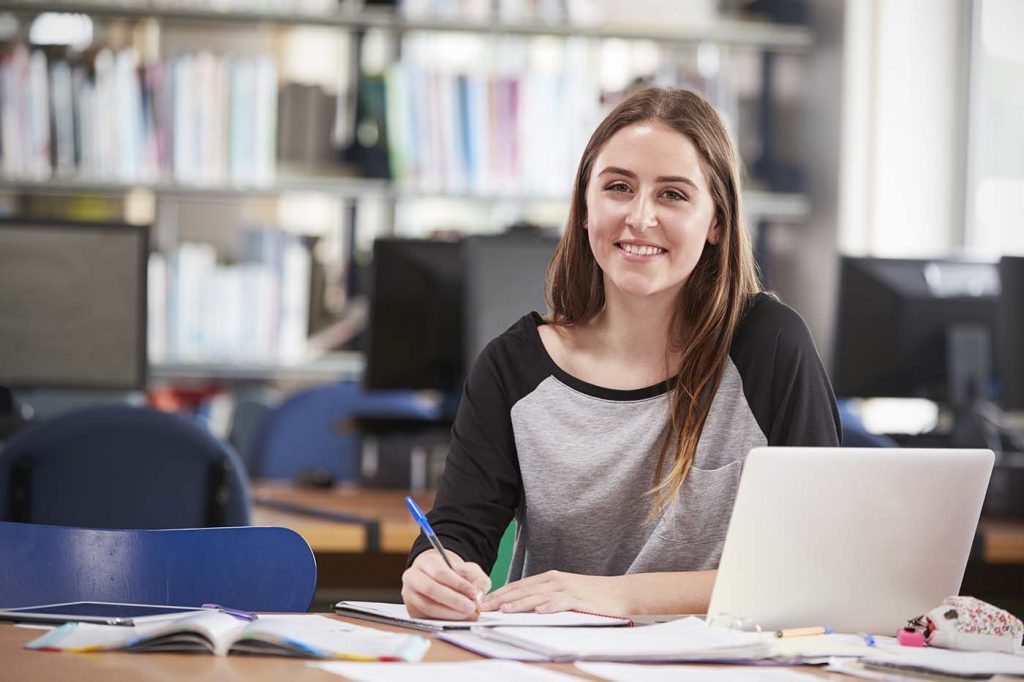 Learner smiling while working on her laptop and surrounded by paper