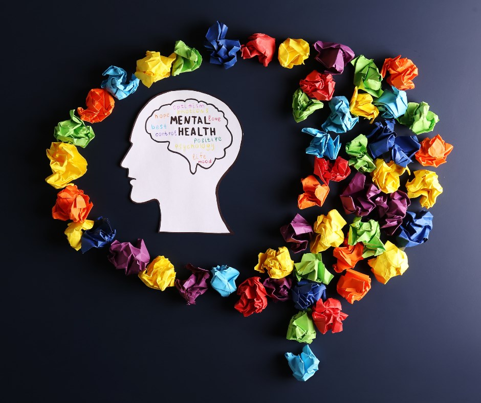 Mental Health sign while surrounded by multicoloured paper that is shaped like a brain