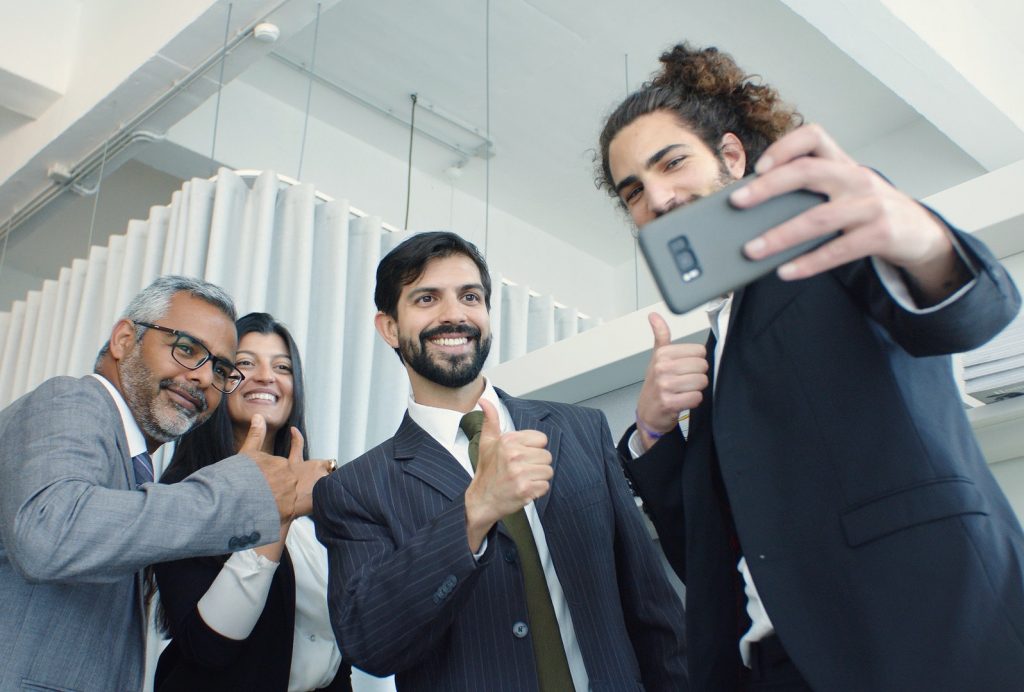 Trainee taking a group selfie at work with everyone smiling and giving a thumbs up